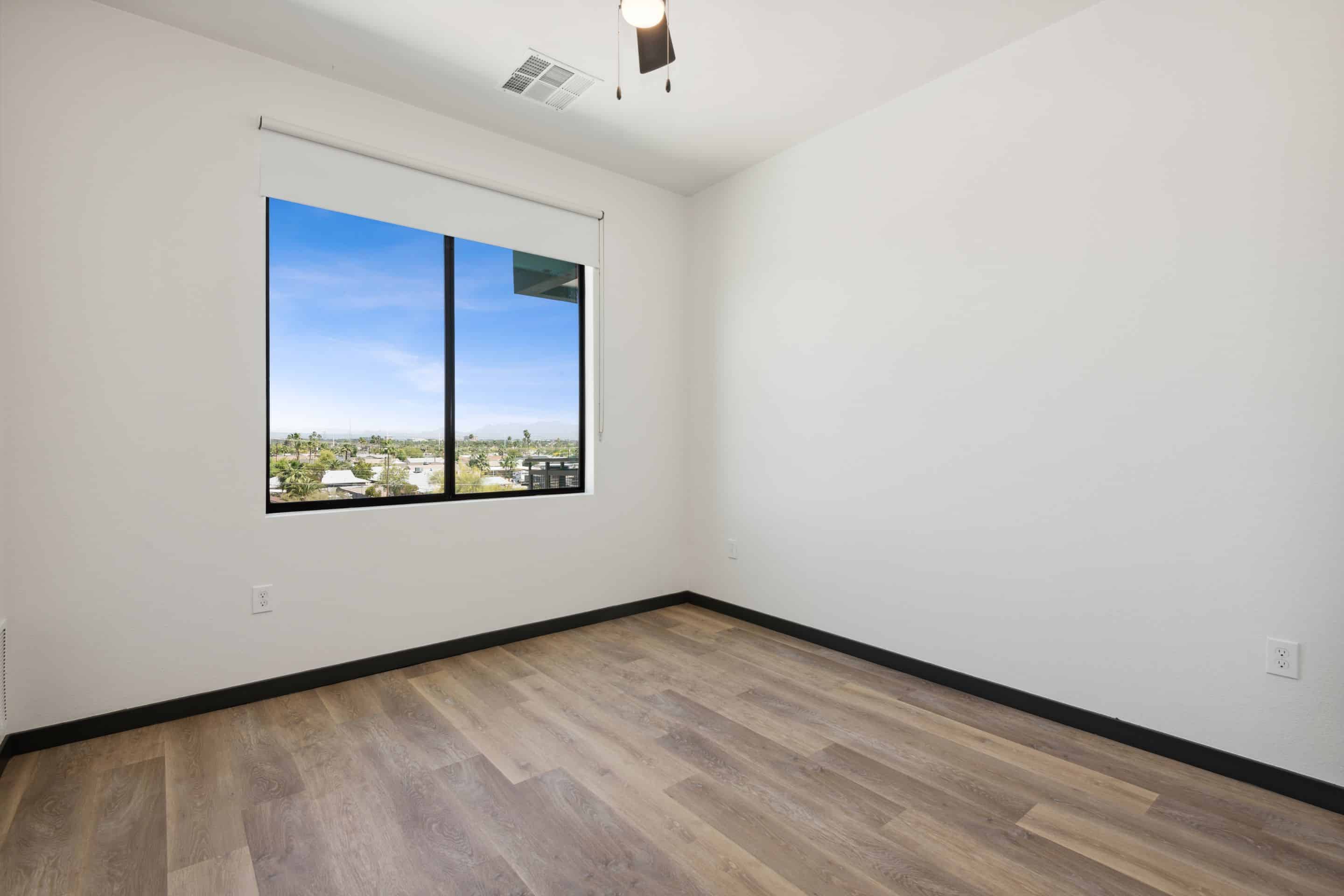 Empty room with light-colored walls, wood-style flooring, a large window offering views outside, and a small ceiling fan—perfect for making Home at Lake Cameron.