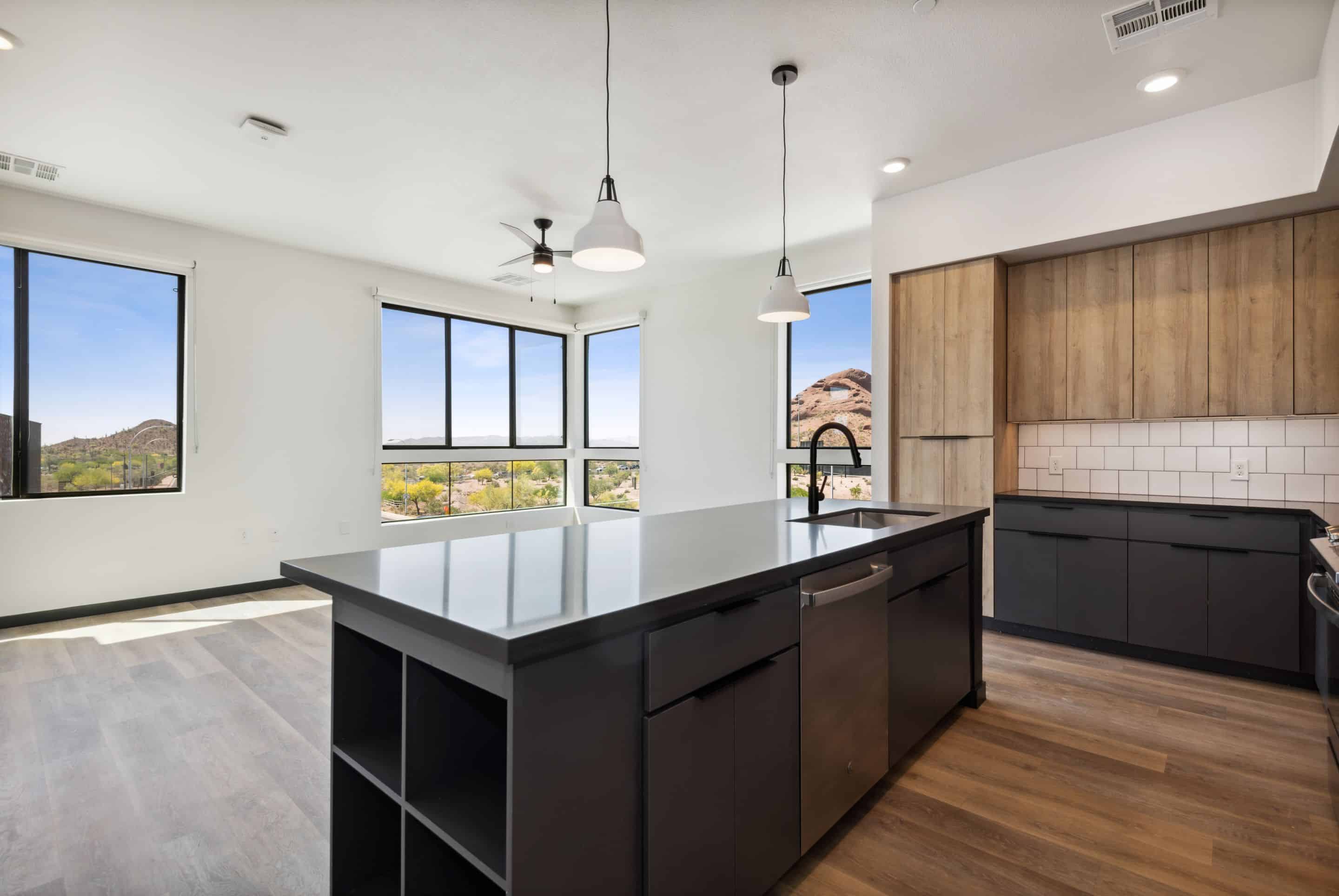 Modern kitchen with black island, wood flooring, built-in appliances, and large windows offering mountain views in a bright open-plan living space—an inviting Home at Lake Cameron.
