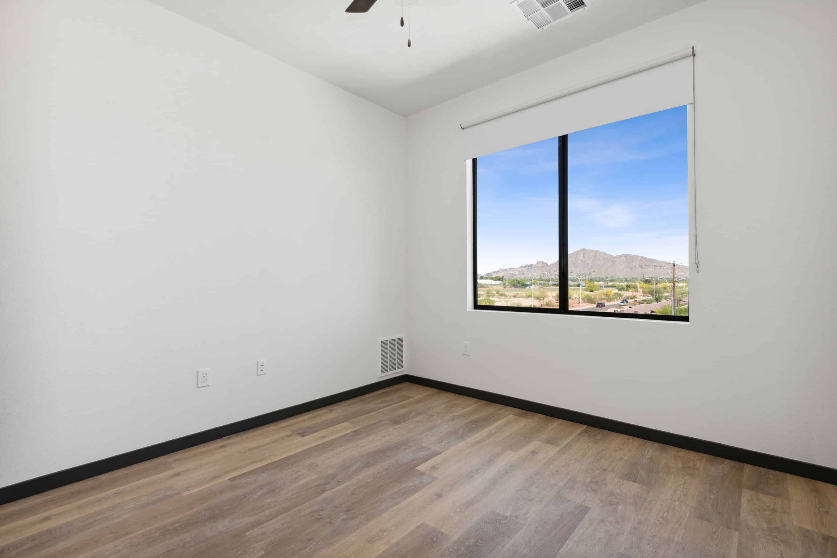 Empty room with light wood flooring, white walls, a ceiling vent, and a large window showcasing mountain views and a clear sky—perfect for your Home at Lake Cameron.