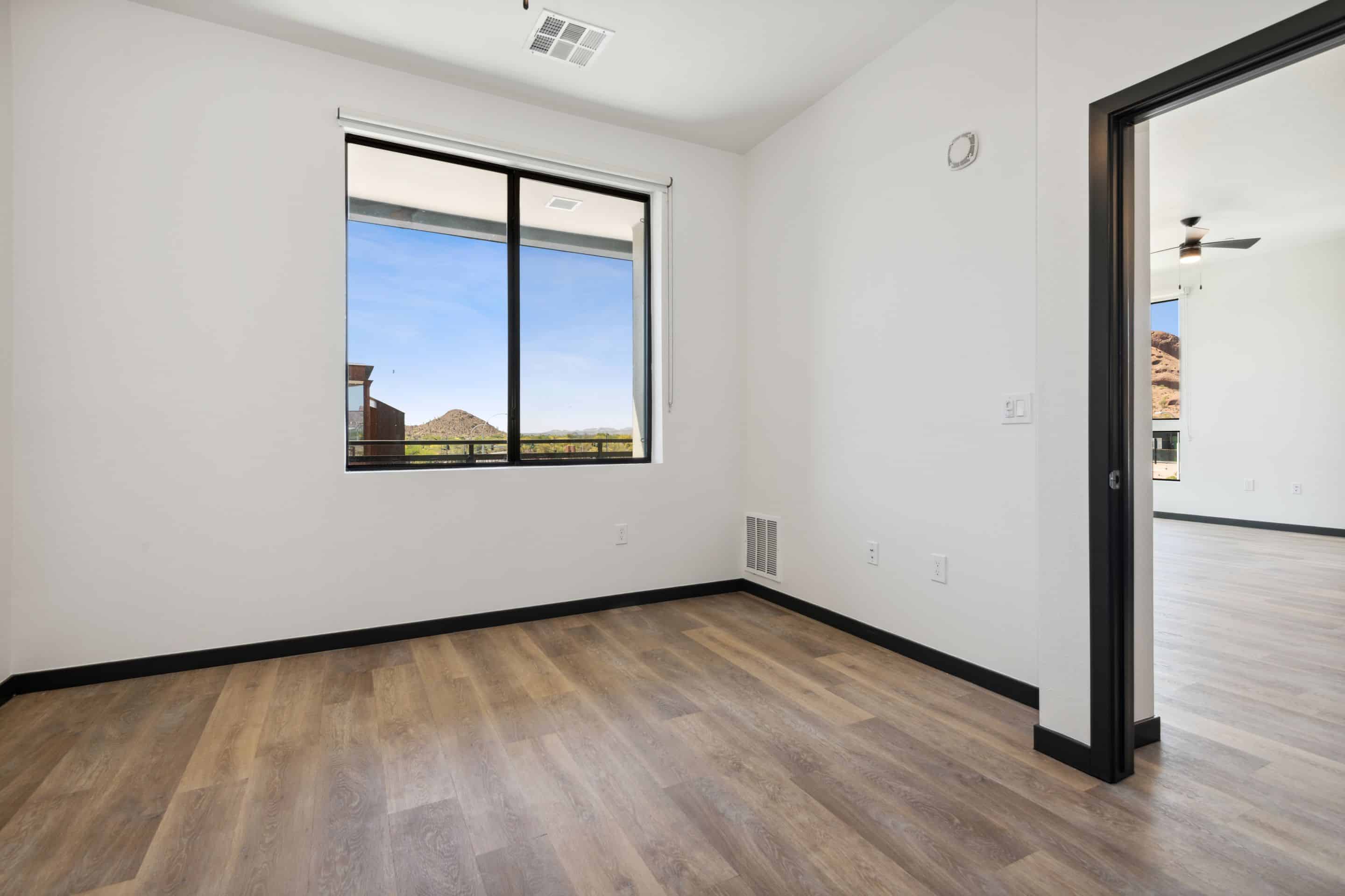 Empty room with white walls, wood-style flooring, and a large window offering views outside—this inviting space at Home - Lake Cameron features an open doorway leading to another area.