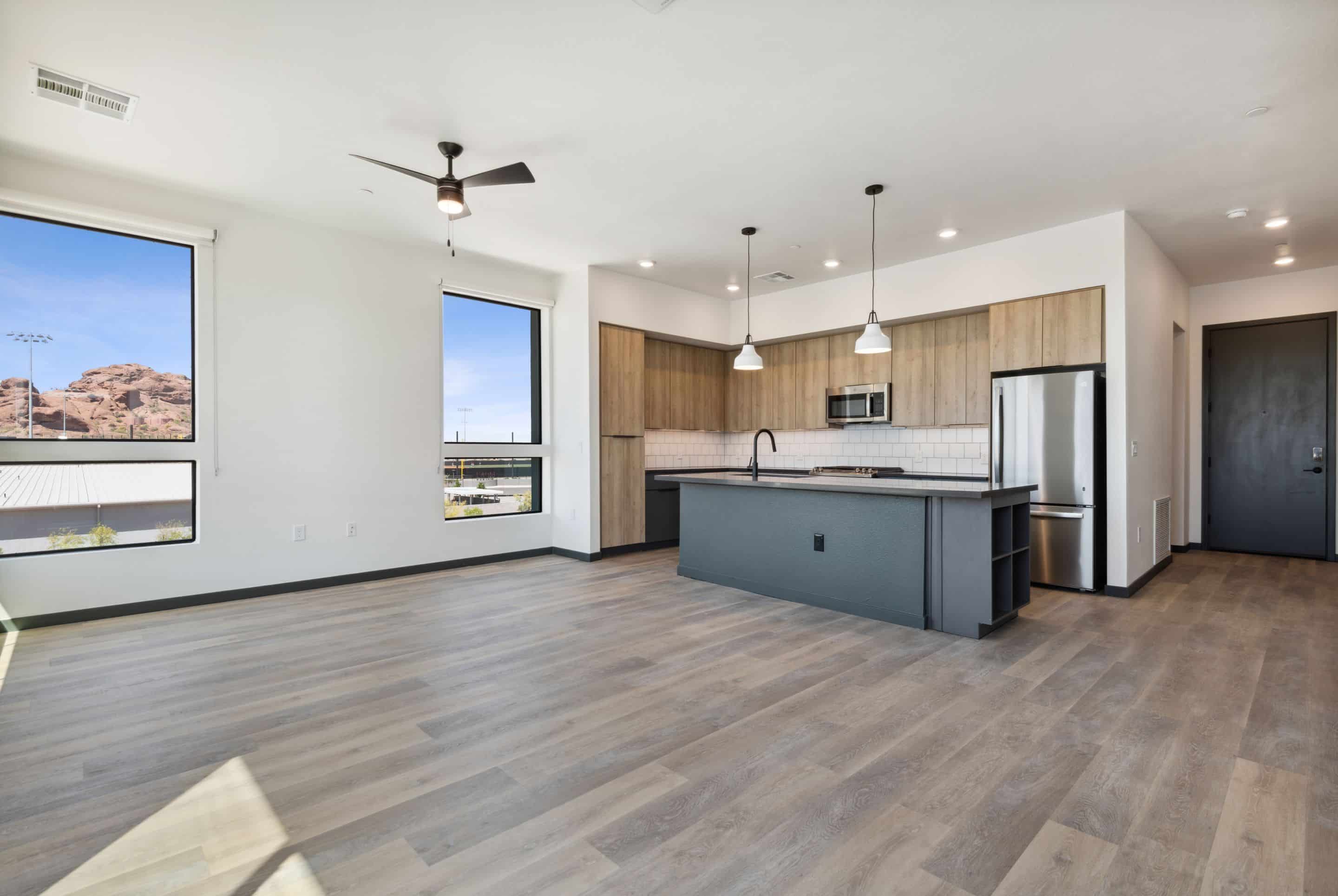 Modern open-concept kitchen and living area in this Lake Cameron home, featuring wood flooring, large windows, light wood cabinets, a black island, and stainless steel appliances.