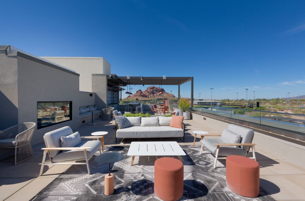 A modern rooftop patio at Home - Lake Cameron features outdoor seating, tables, a rug, and mountain views under a clear blue sky.