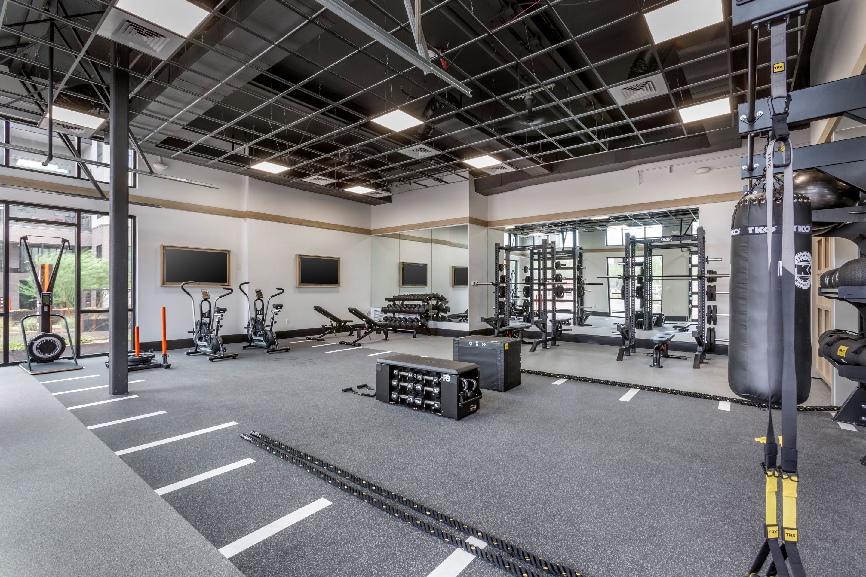 Modern gym with cardio machines, free weights, squat racks, and various fitness equipment in a spacious, well-lit room with large windows and high ceilings—perfect for residents at Home - Lake Cameron.