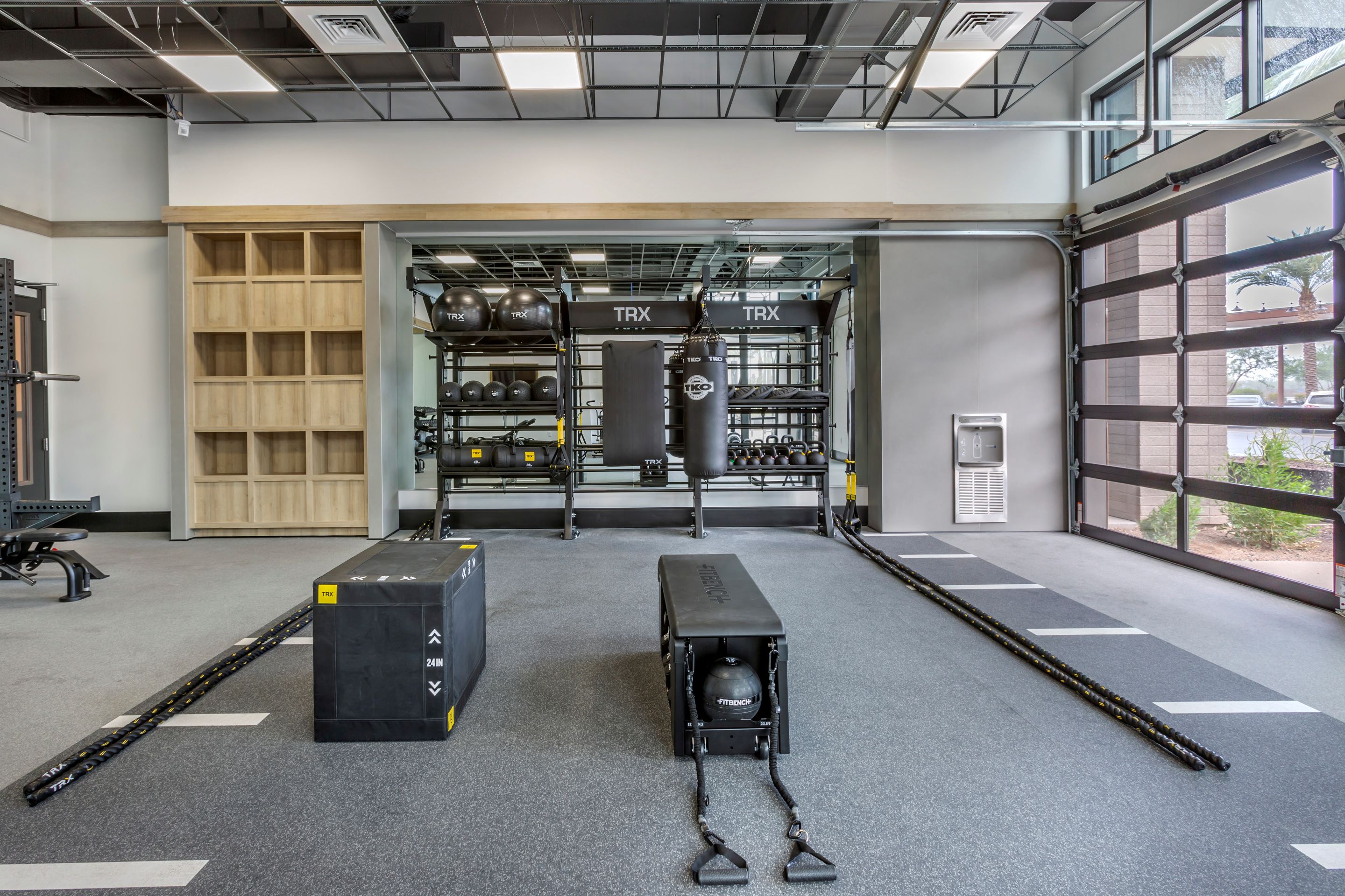 Modern gym space at Home - Lake Cameron featuring TRX suspension trainers, medicine balls, plyometric boxes, and benches; large windows fill the room with natural light.