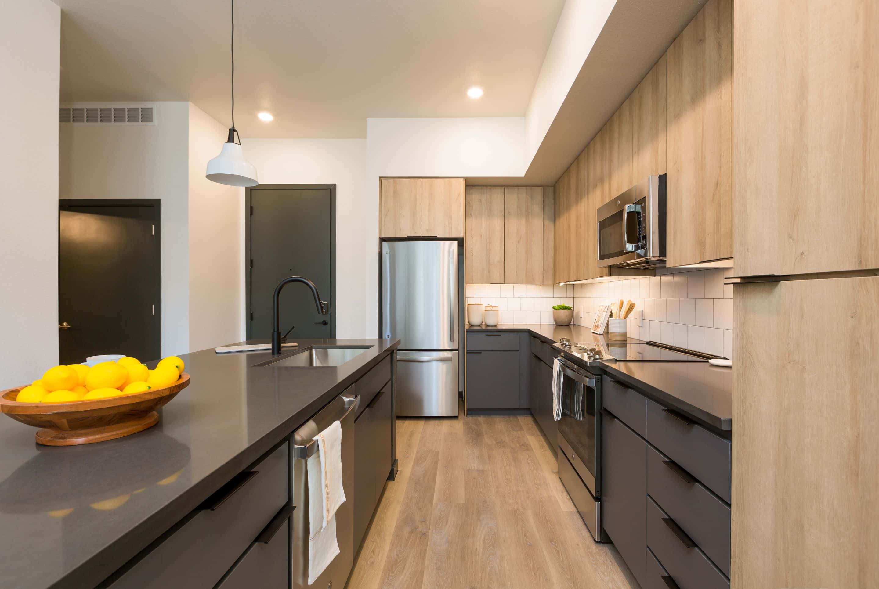 Modern kitchen in Home - Lake Cameron with wood and dark cabinets, stainless steel appliances, a bowl of lemons on the island, and under-cabinet lighting.