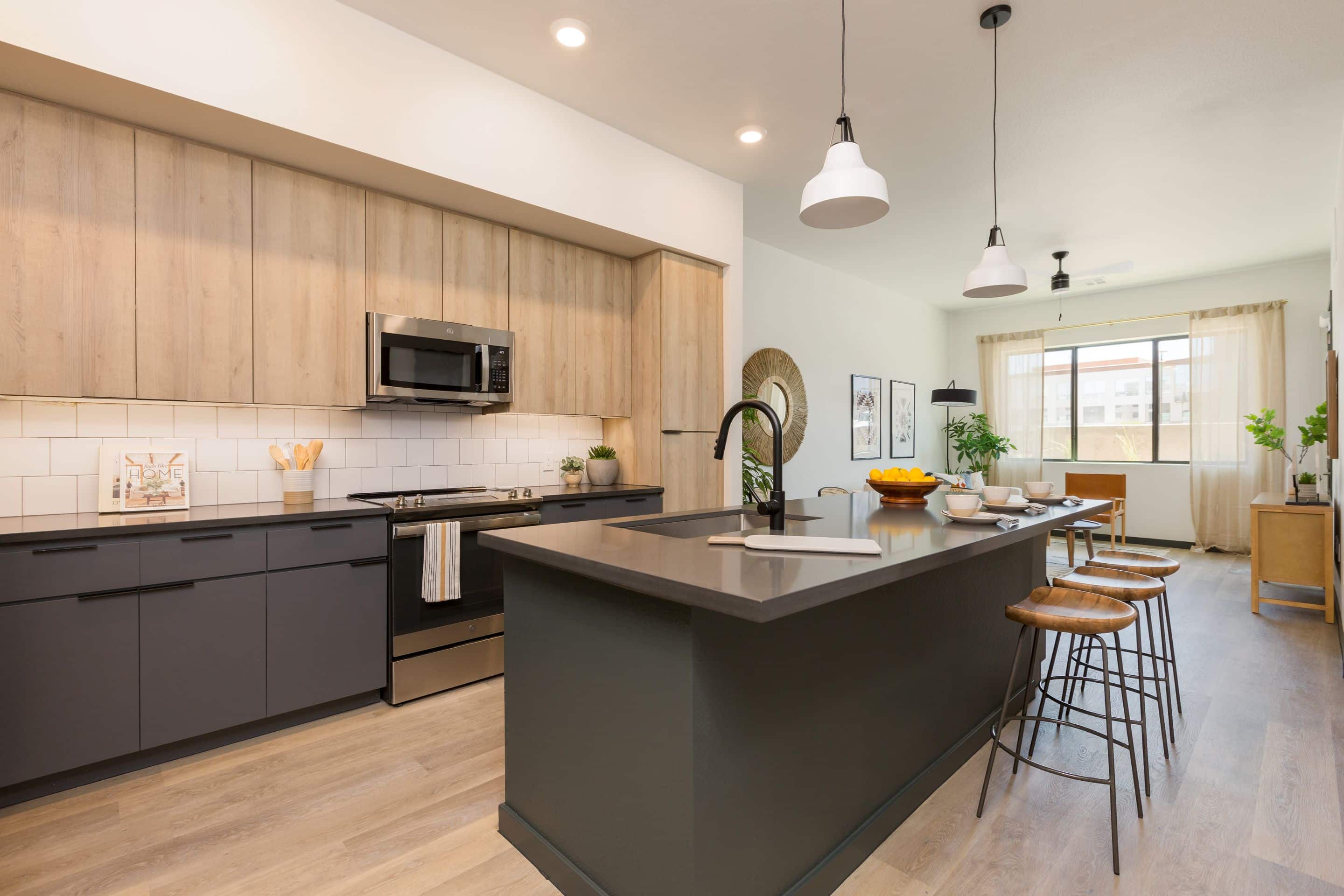 Modern kitchen with black island, wood cabinets, stainless steel appliances, pendant lights, and barstools; dining area overlooks Lake Cameron through a large window, blending style and comfort in this inviting home.