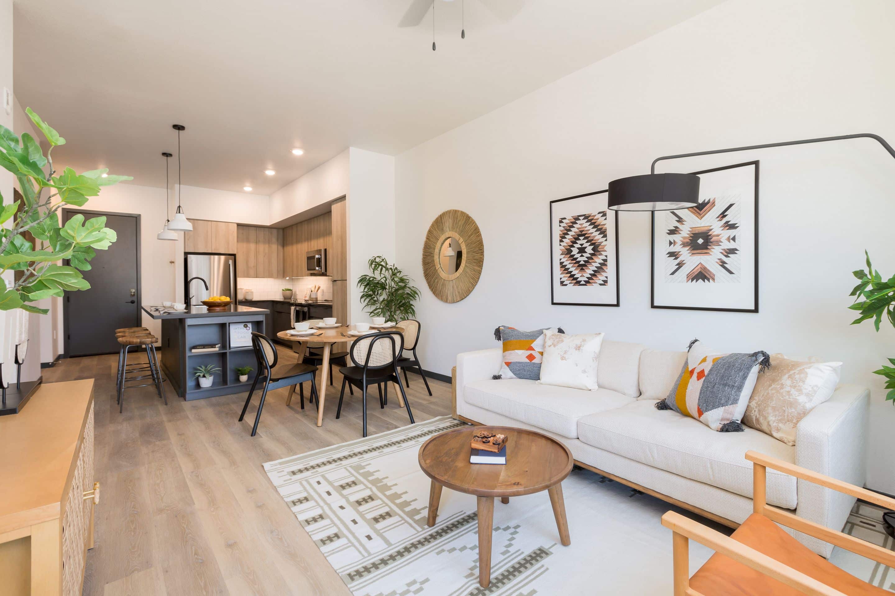 Modern open-concept living room and kitchen in Home - Lake Cameron, featuring light wood flooring, white walls, a beige sofa, round coffee table, dining area, and contemporary decor.