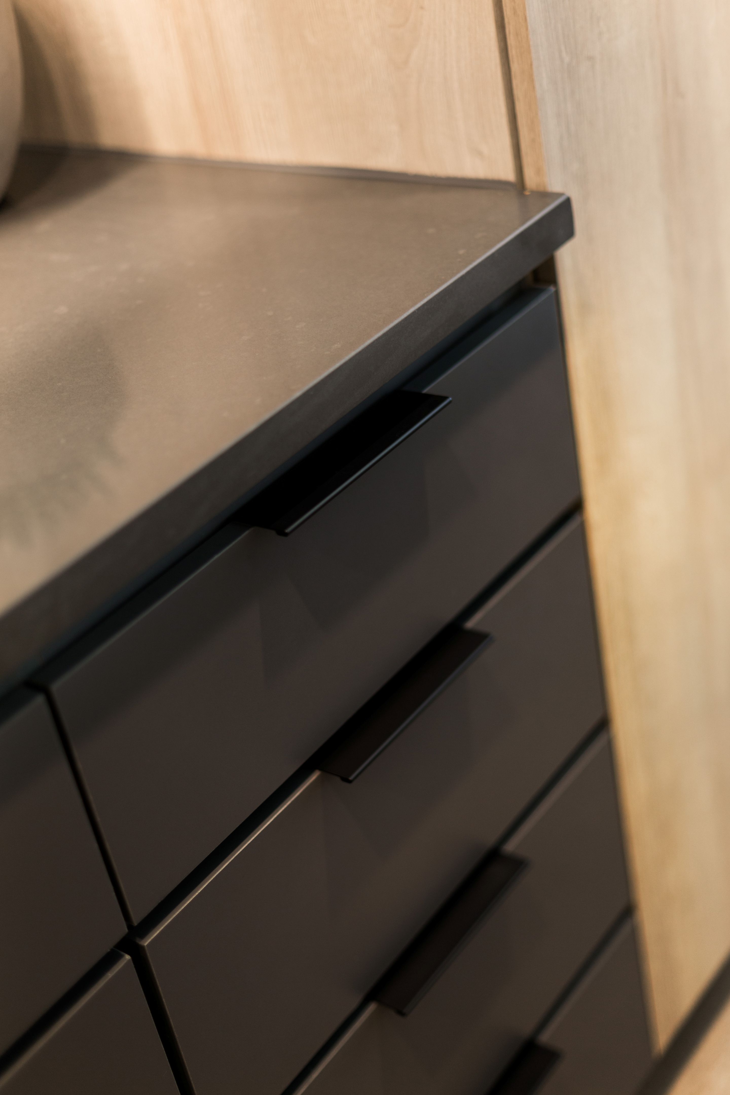 Close-up of matte black drawers with modern handles, set under a smooth, dark countertop and light-colored wooden paneling in this Home - Lake Cameron.