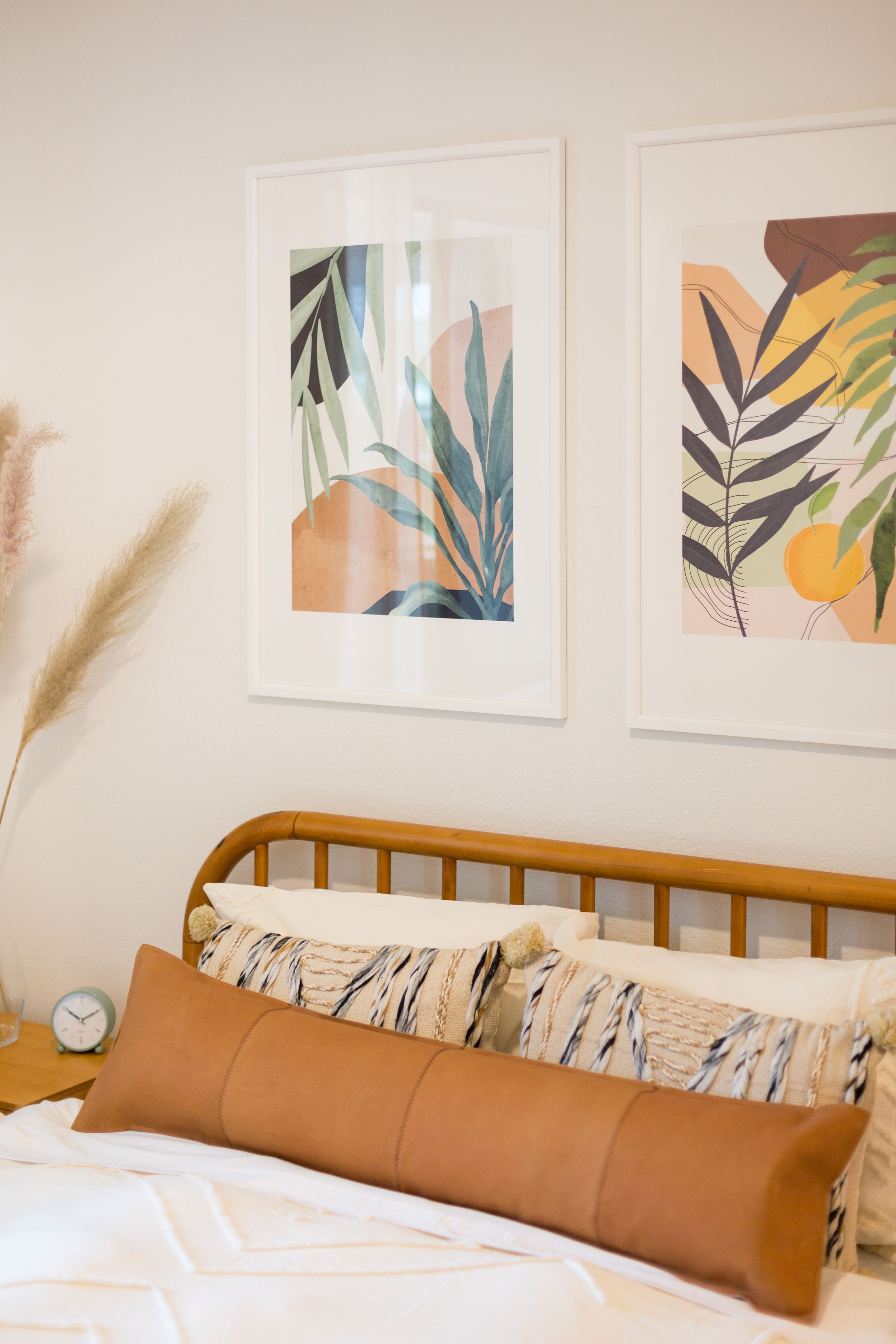 A neatly made bed with patterned pillows and a long brown cushion sits below two framed botanical prints on a light-colored wall, creating a cozy retreat in Home - Lake Cameron.