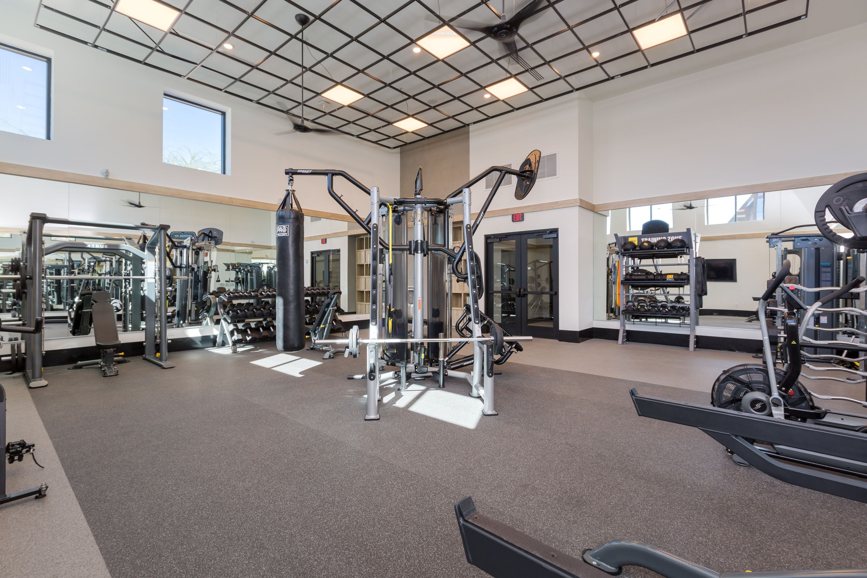 Modern gym at Home - Lake Cameron with various exercise equipment, including a punching bag, weight machines, and benches, set in a brightly lit room featuring large windows and mirrors.