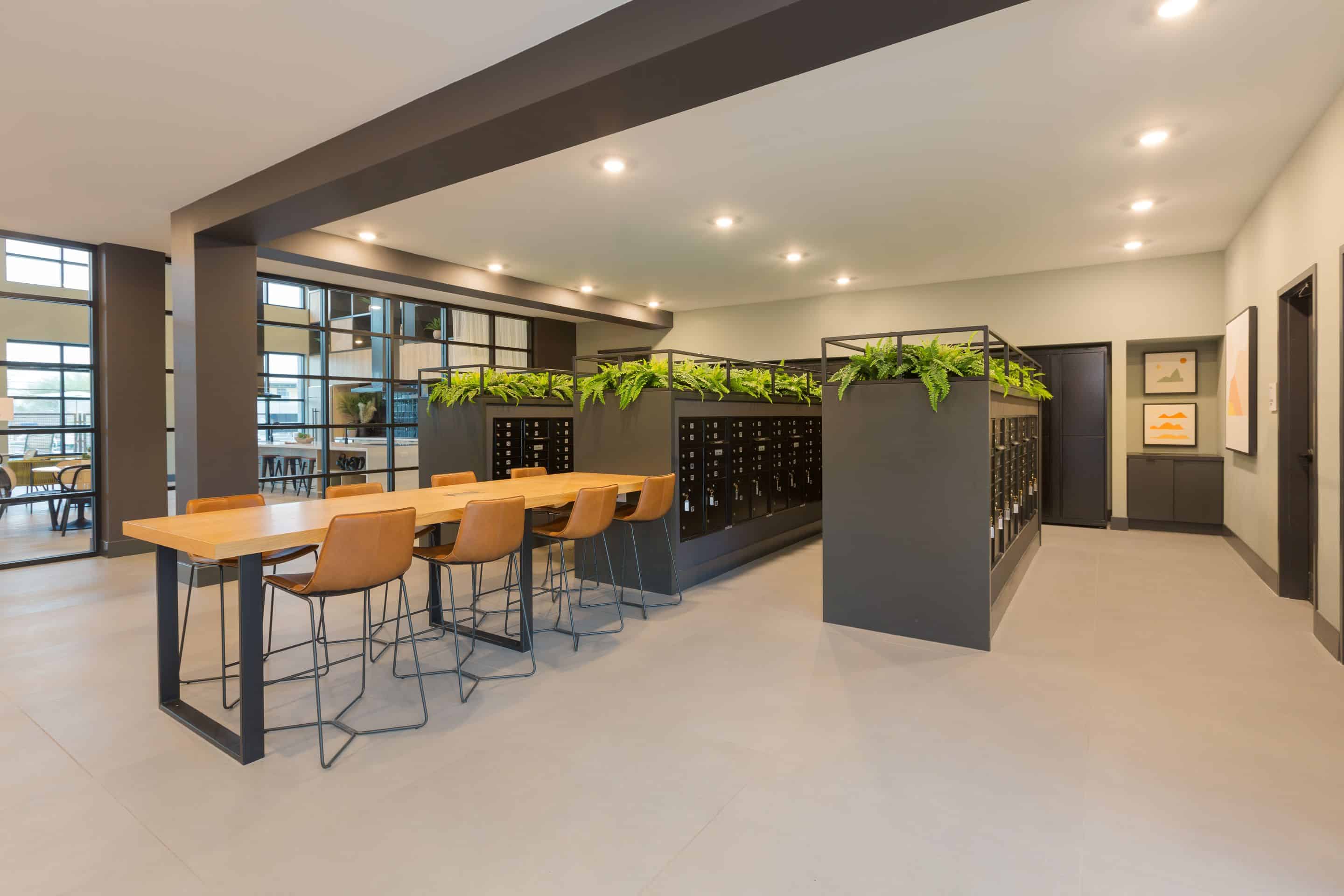 Modern office space at Home - Lake Cameron featuring a long wooden table, several chairs, black cabinets adorned with green plants, and framed art on the walls.