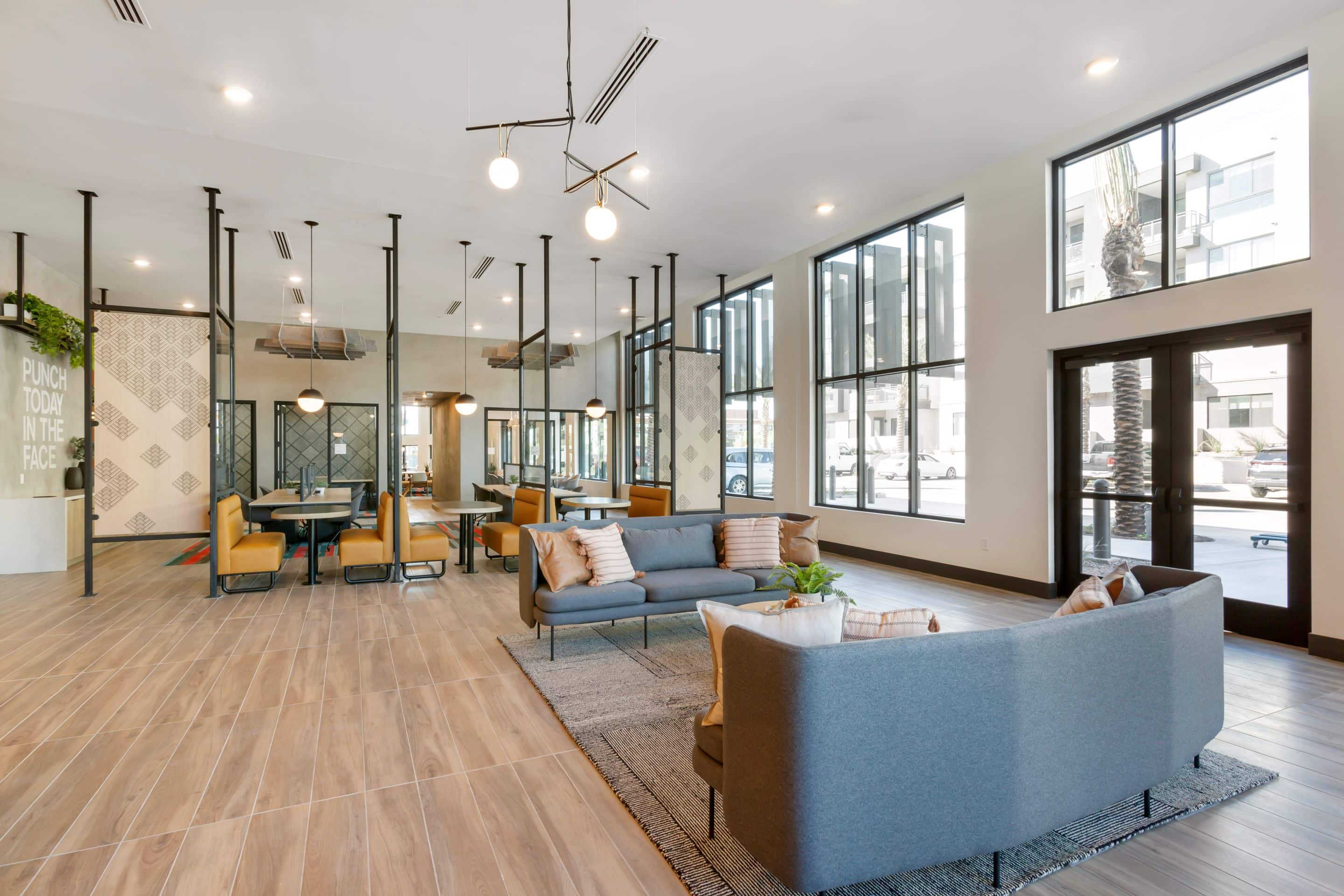 Modern, spacious lounge area at Home - Lake Cameron features large windows, wood flooring, contemporary furniture, and multiple seating areas arranged for socializing and work.