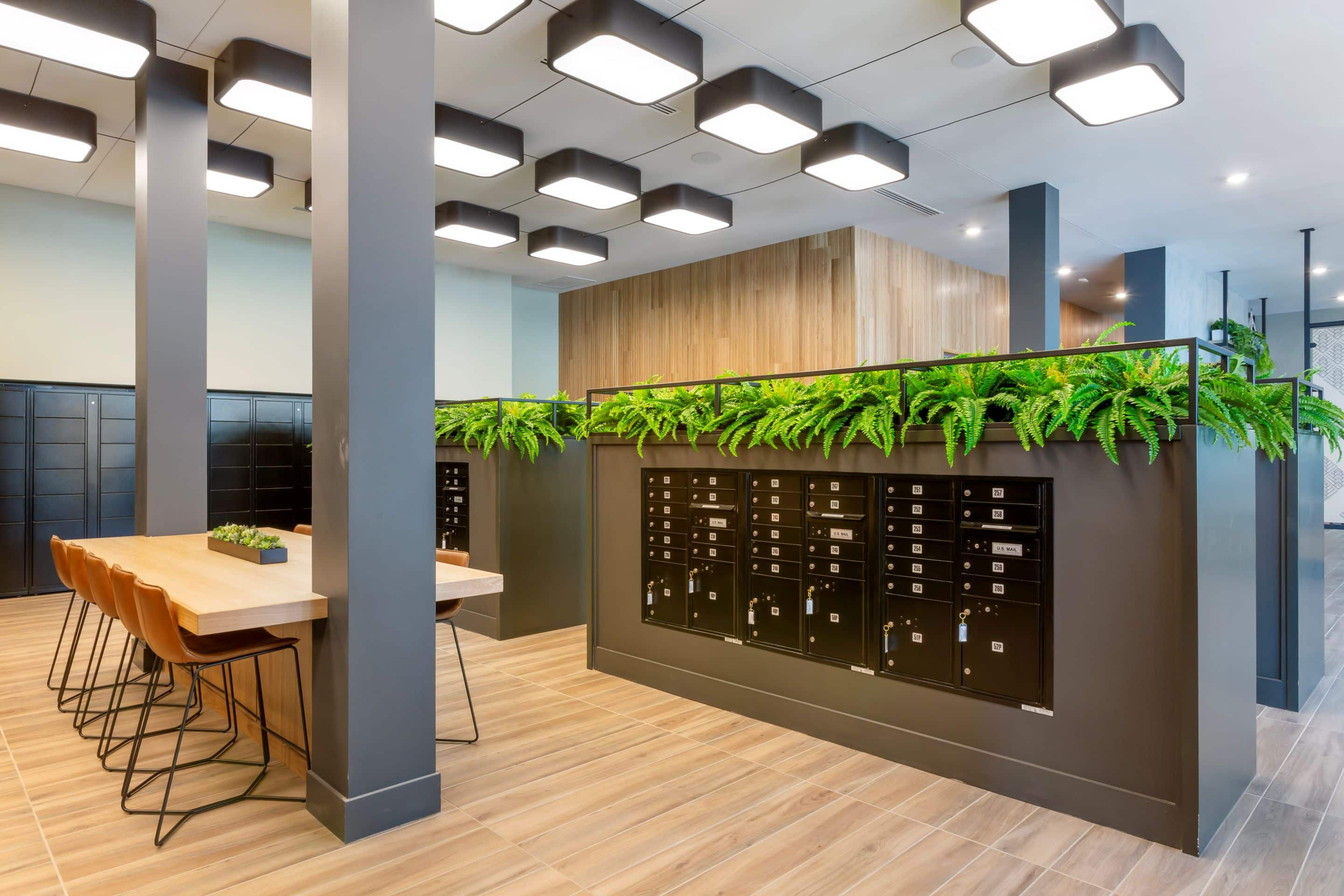 Modern office space with a wooden table and chairs on the left, black mailboxes and green ferns on the right, and geometric ceiling lights above—perfect for working from your Home - Lake Cameron retreat.
