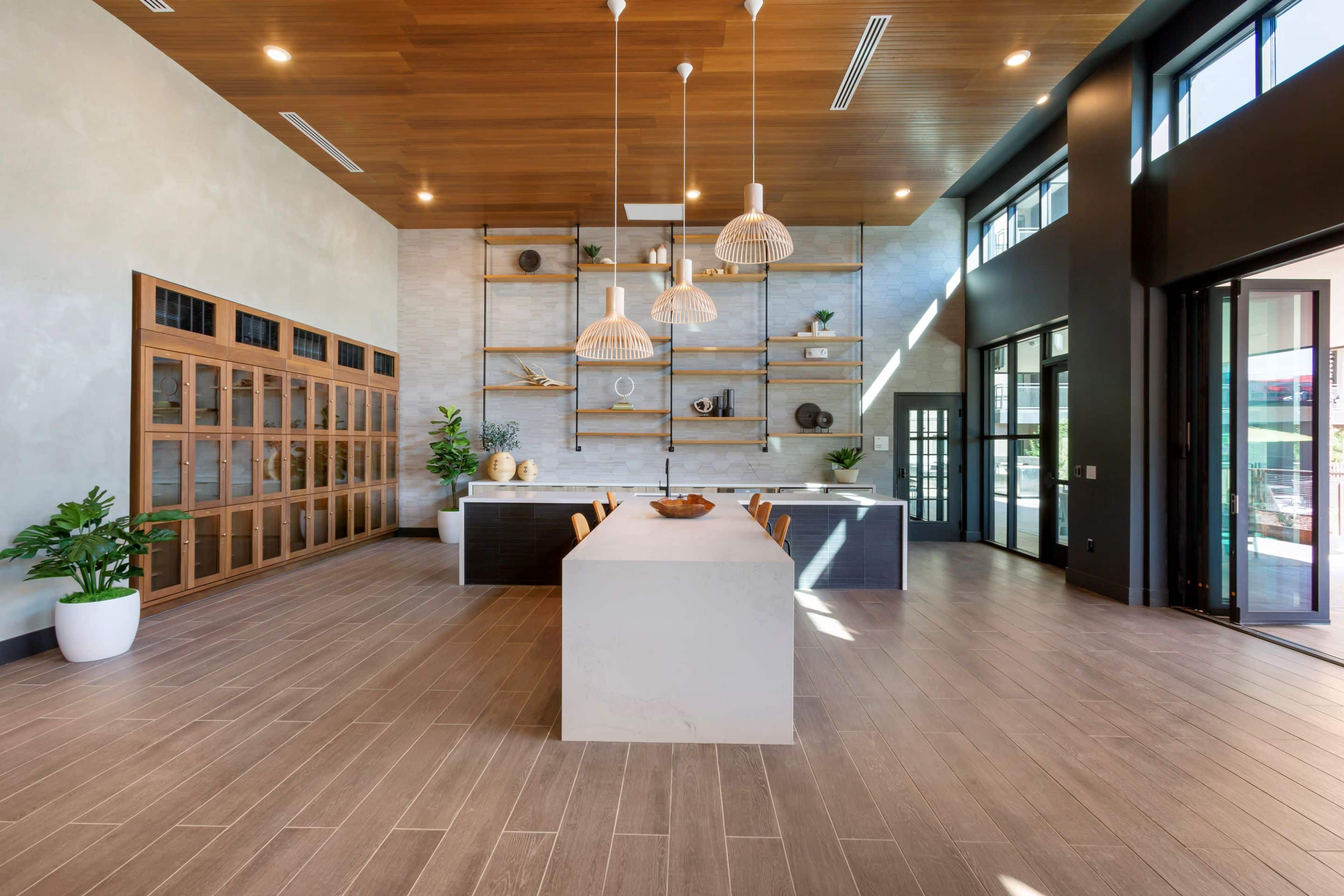 Modern kitchen at Home - Lake Cameron features a large island, pendant lights, wooden ceiling, open shelving, and expansive windows; indoor plants in white pots add a fresh touch.