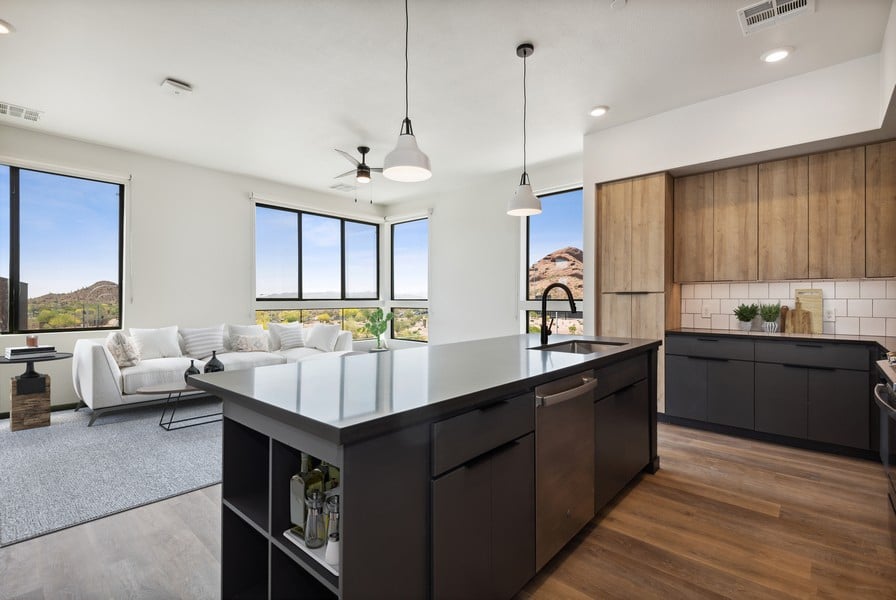 Modern open-concept kitchen and living room at Scottsdale Entrada, featuring large windows, a black island, wood cabinetry, and stunning mountain views outside.