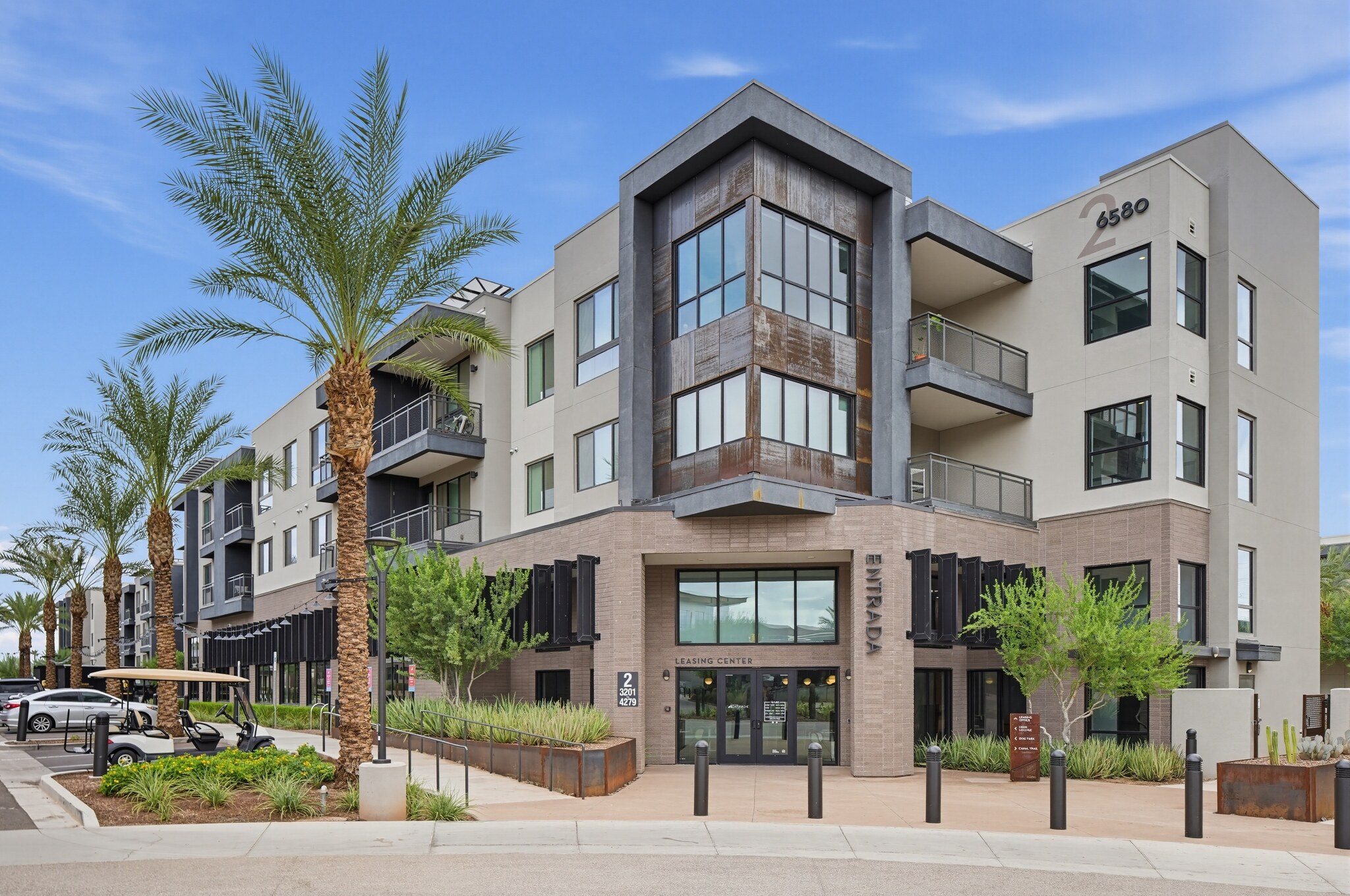 Modern three-story apartment building with balconies, palm trees, and glass entrance. The address 4580 is displayed on the corner of the upper floor. Sky is clear.